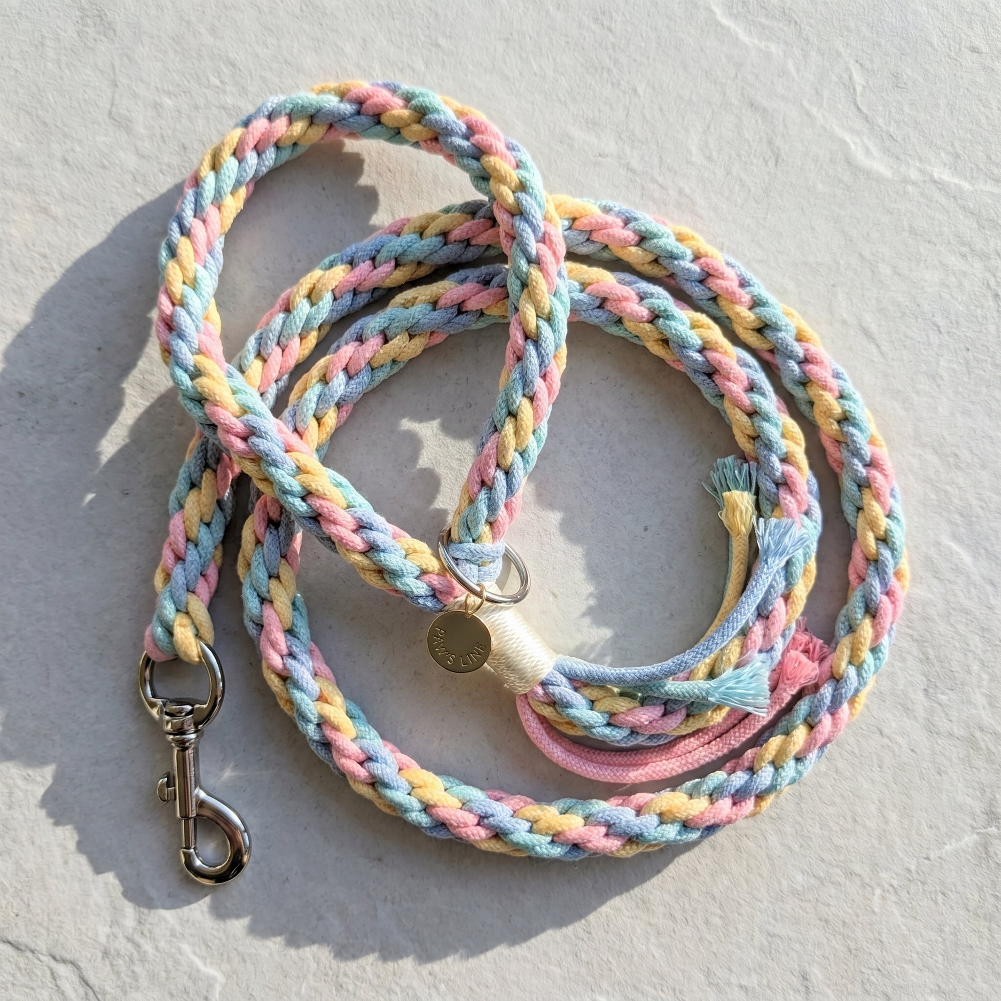 The hand-woven cotton rope dog leash in Cotton Candy Swirl by Paw's Line, coiled neatly on a textured slate studio background. color:Cotton Candy Swirl