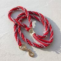The Traverse Braided Paracord Leash in Crimson Trail by Paw's Line, coiled on a textured slate background with gold hardware. color:Crimson Trail