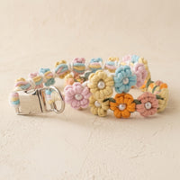 The Pearl & Blossom Floral Dog Collar by Paw's Line, loosely looped to show its premium metal side-release buckle on a textured matte cream studio background.