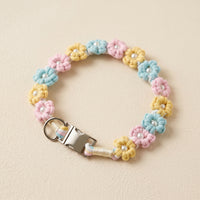 Paw's Line macrame flower dog collar. color:Pastel Candy. Displayed as a standalone loop on a warm cream backdrop with a metal buckle.