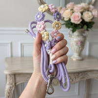 A woman holding a coiled pastel purple rope dog leash with a flower macrame handle and silver Paw's Line logo tag in an elegant home entryway.