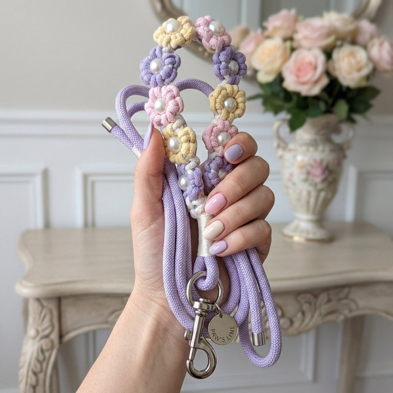 A woman holding a coiled pastel purple rope dog leash with a flower macrame handle and silver Paw's Line logo tag in an elegant home entryway.
